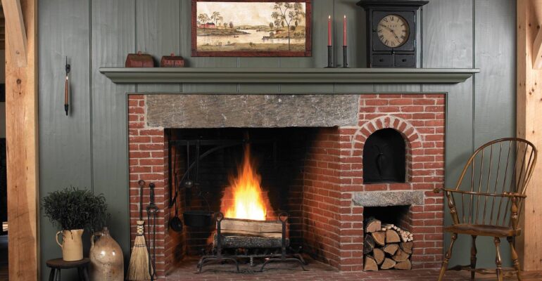 A glowing fire in a huge brick fireplace with big granite lintel stone and beehive oven