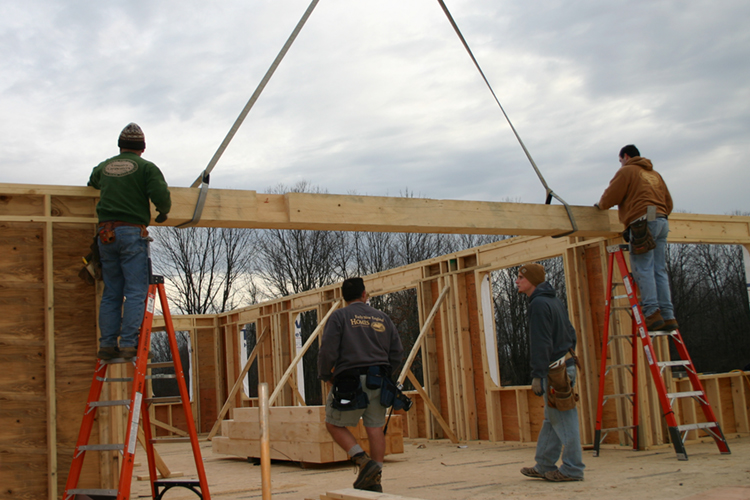 A team of carpenters from Early New England Homes raise a  beam.